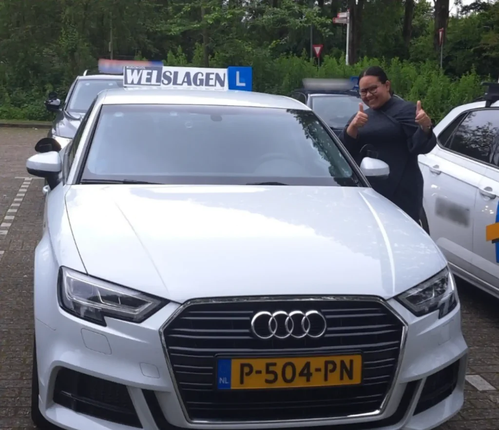 Geslaagde leerling toont duimen omhoog naast witte Rijschool Welslagen lesauto in Rotterdam