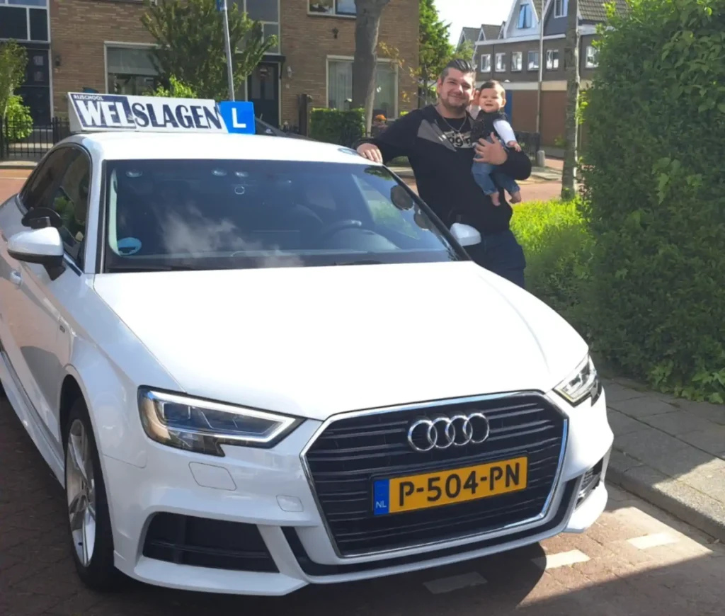 Geslaagde man met baby bij witte Audi rijscholauto van Rijschool Welslagen na succesvol behalen rijbewijs Geslaagde man met baby bij witte Audi rijscholauto van Rijschool Welslagen na succesvol behalen rijbewijs
