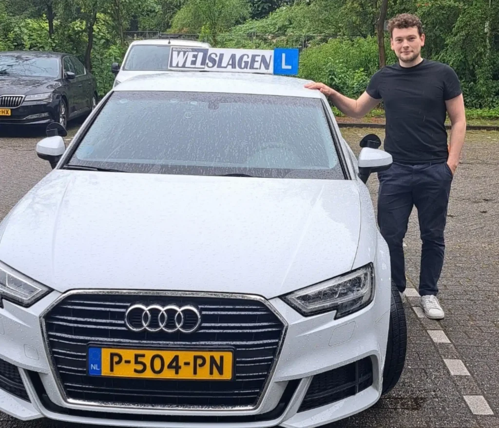 Geslaagde student poseert trots naast leswagen van Rijschool Welslagen na het behalen van zijn rijbewijs